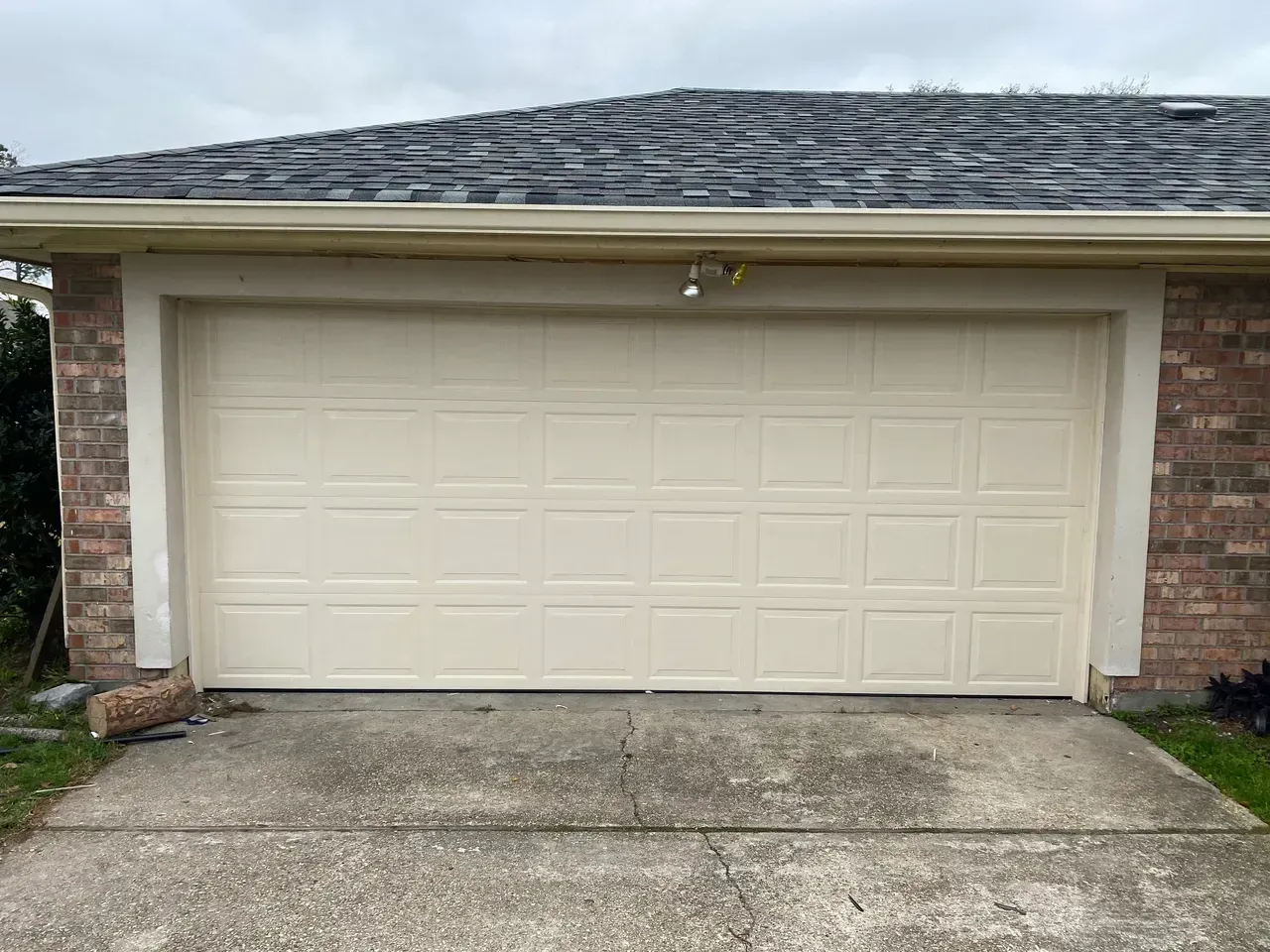 Tan garage door on a concrete driveway, set in a brick and beige frame.