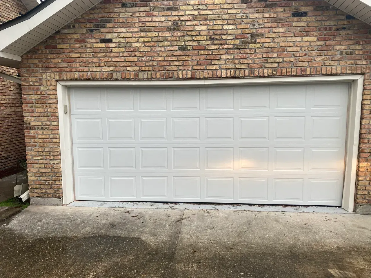 White garage door on a brick building; concrete driveway in front.