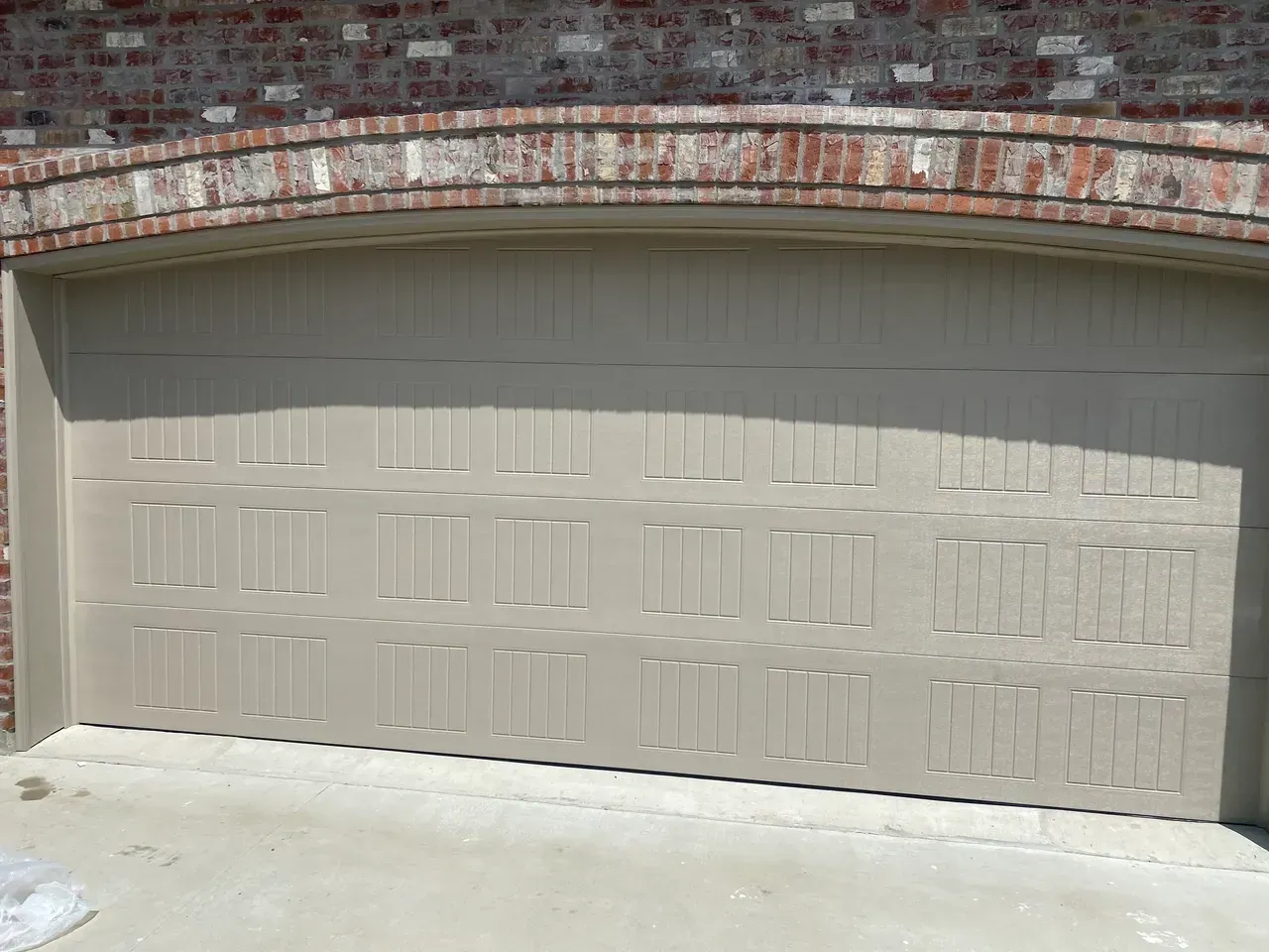 Tan garage door under brick archway.