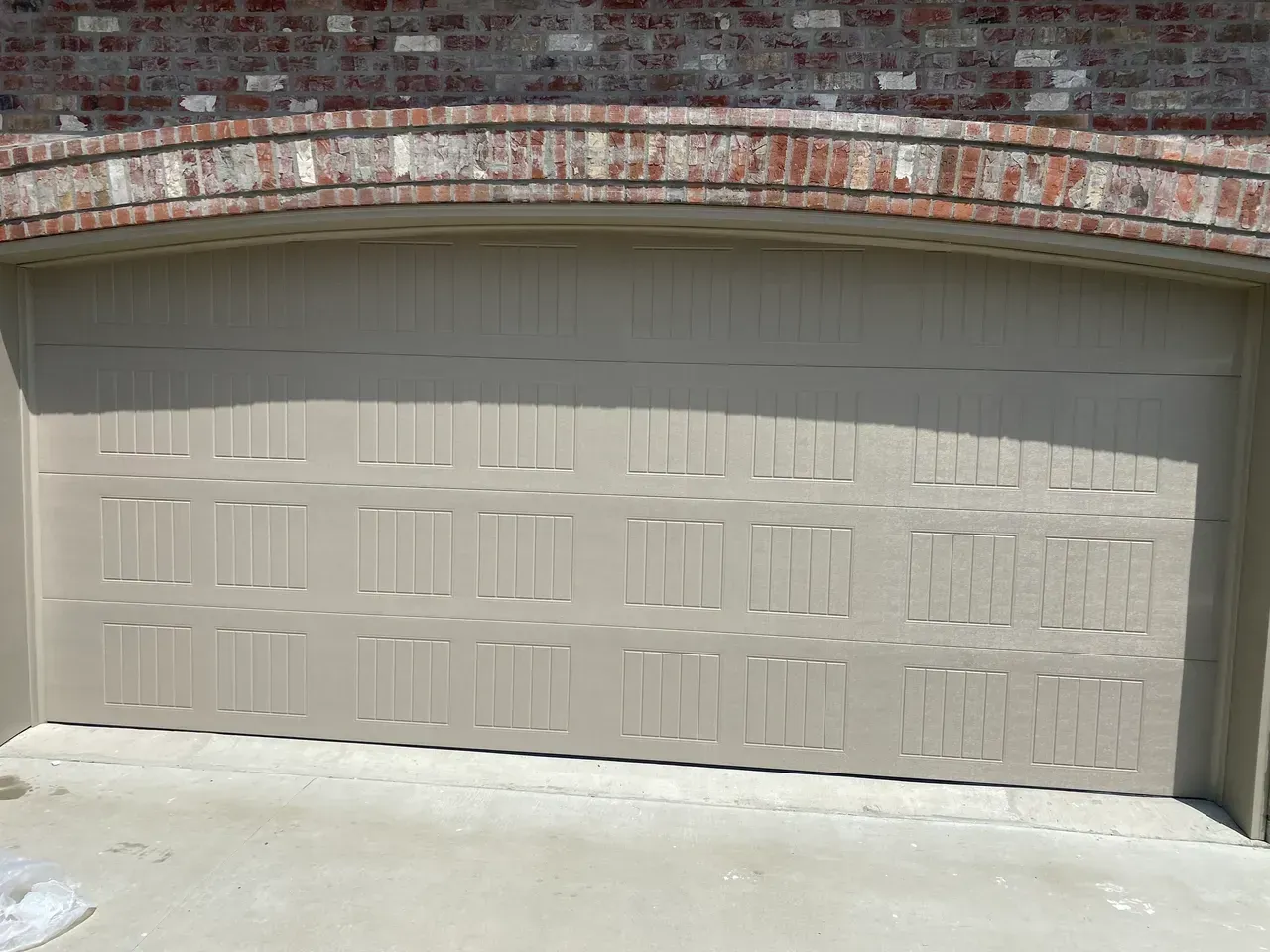 Tan garage door under brick archway.