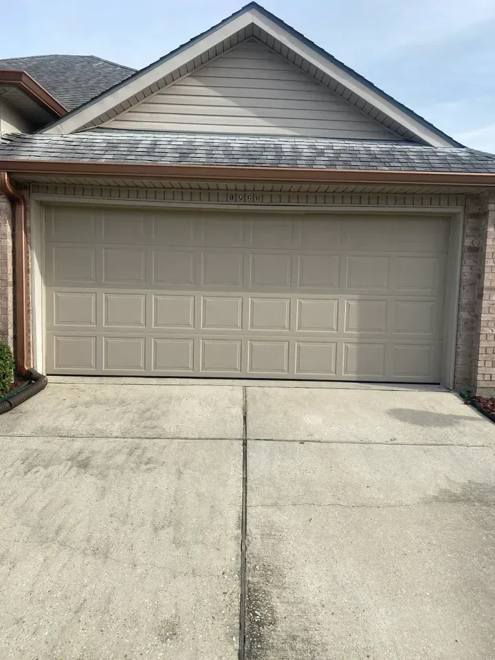 Tan garage door on a concrete driveway, under a brown roof with copper gutters.