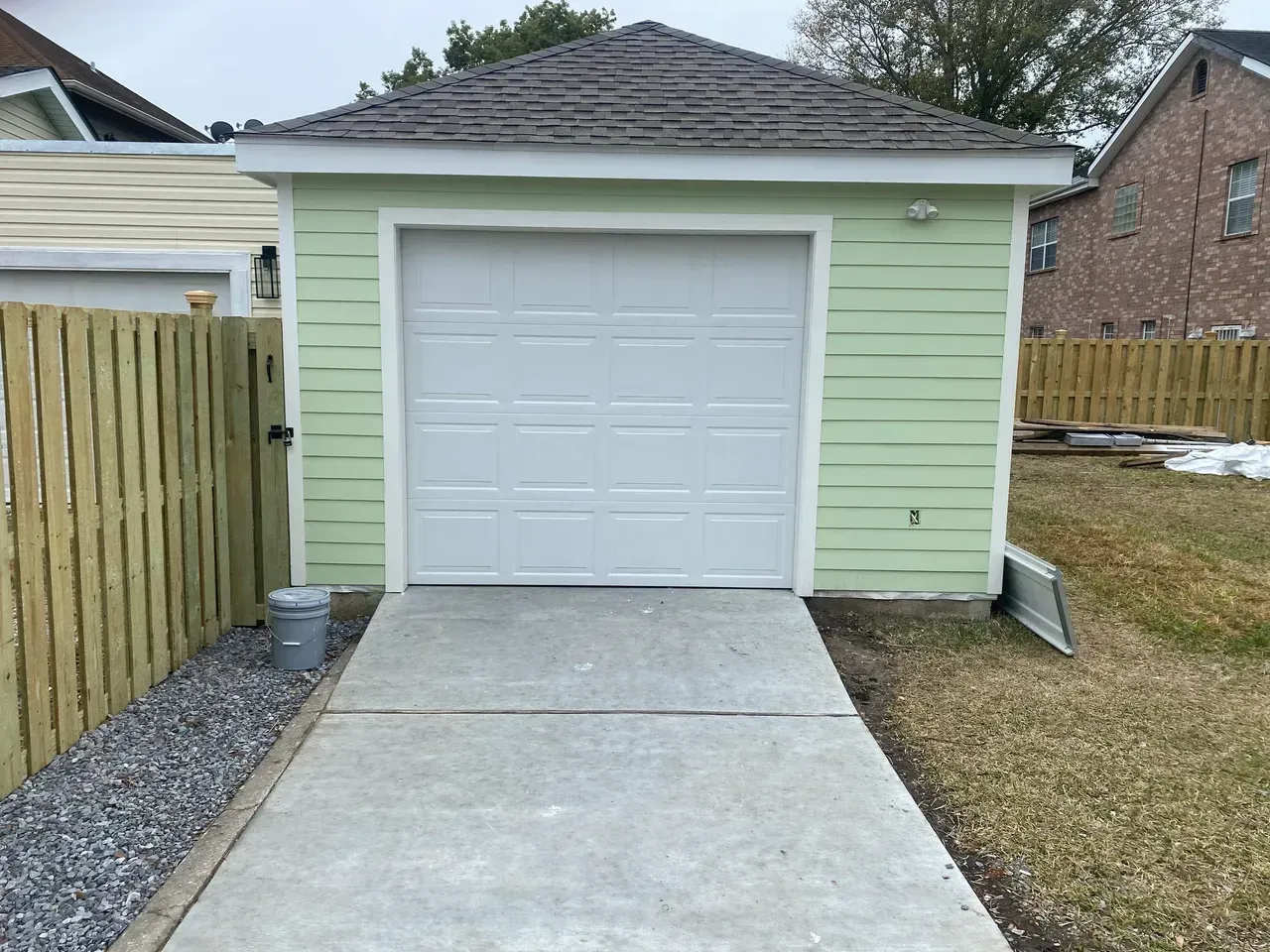 Green-painted detached garage with white door and concrete driveway.
