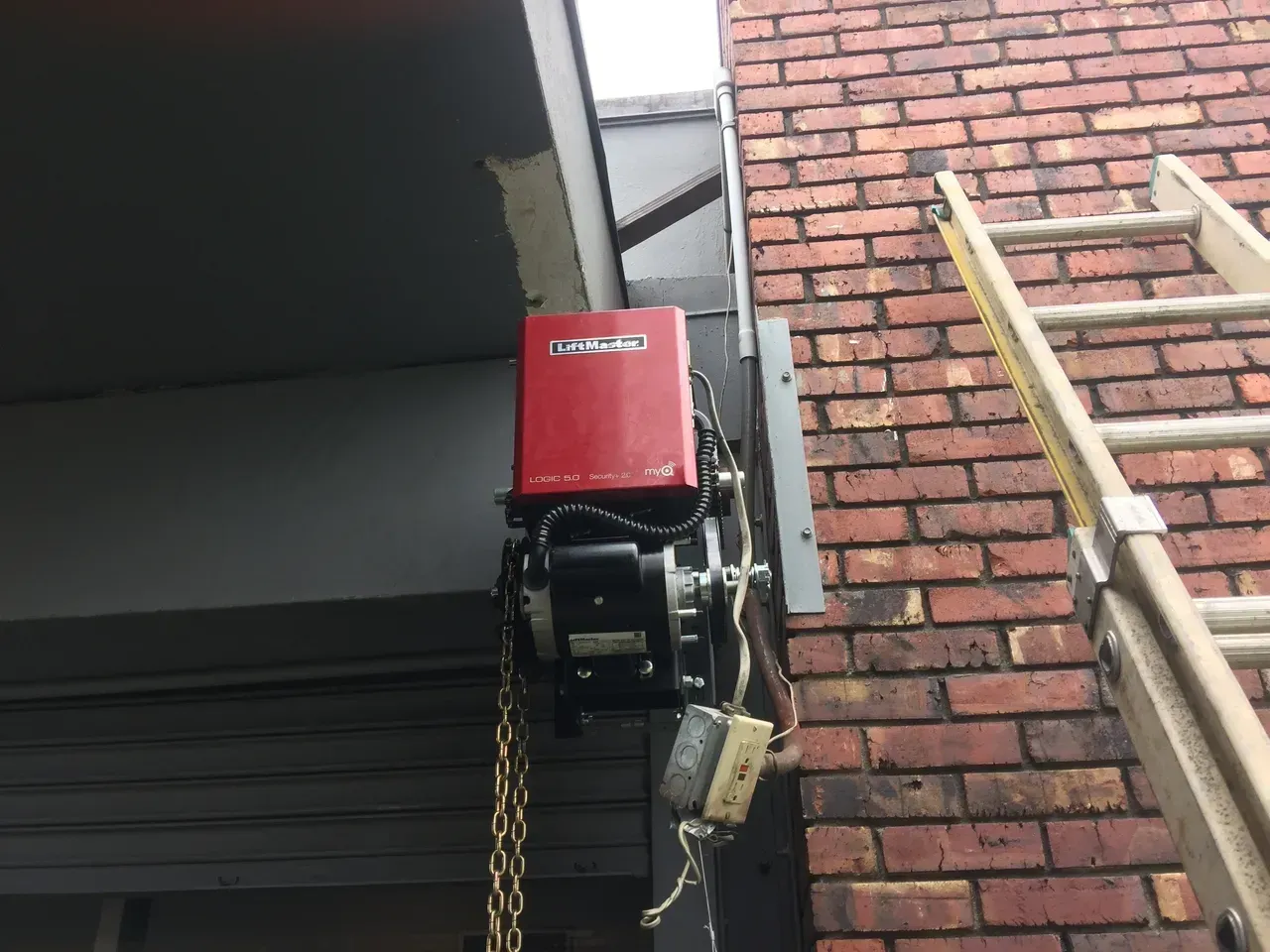 Red gate opener motor mounted on brick wall.