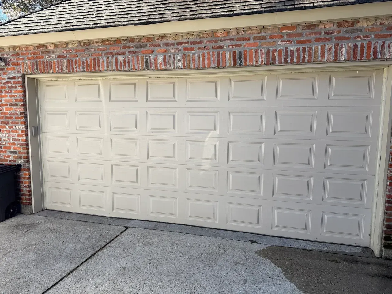 Tan garage door in front of a brick building. Concrete driveway.