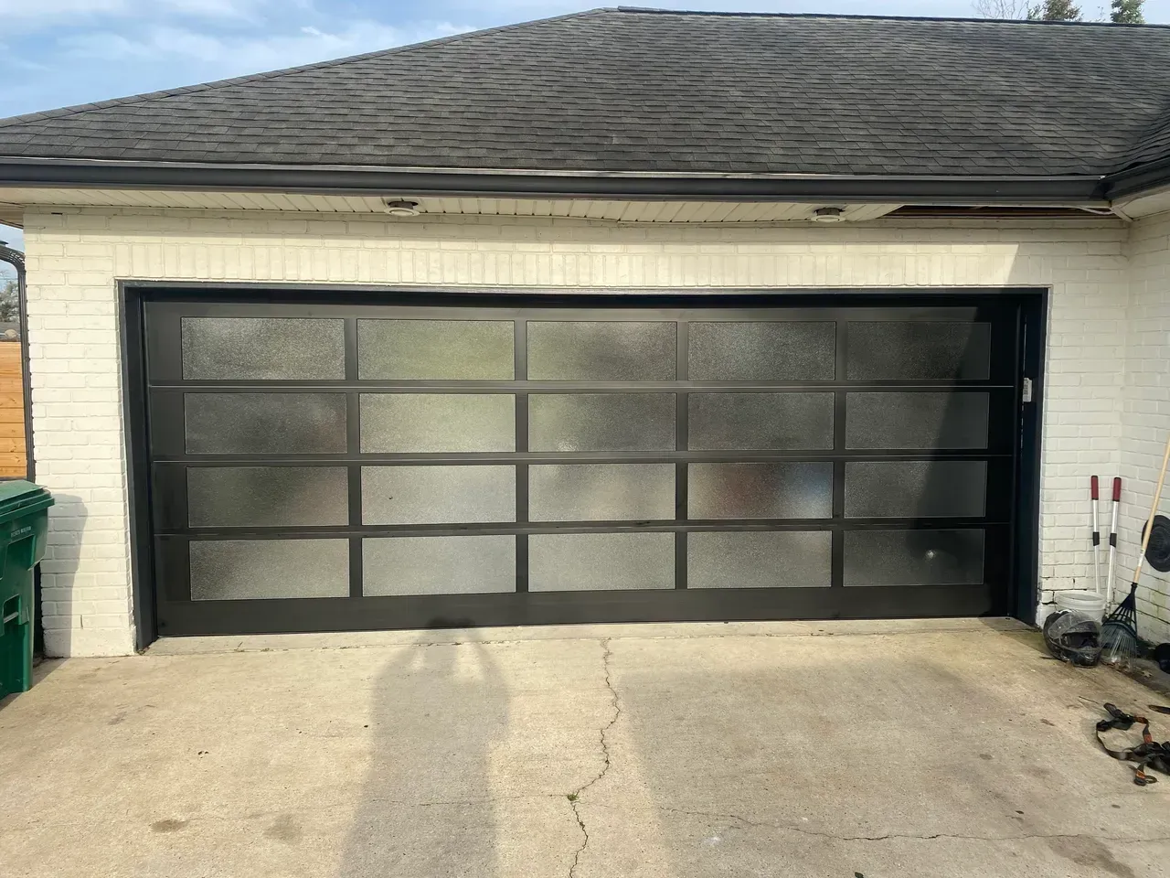Black framed garage door with frosted glass panels, mounted on a white brick building.