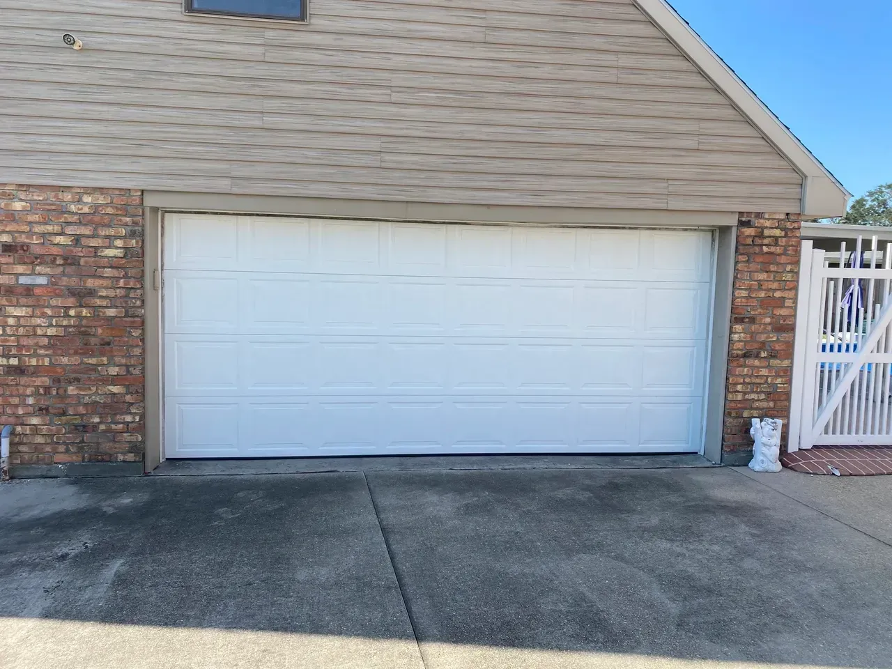 White garage door on a brick and siding building, with concrete driveway.