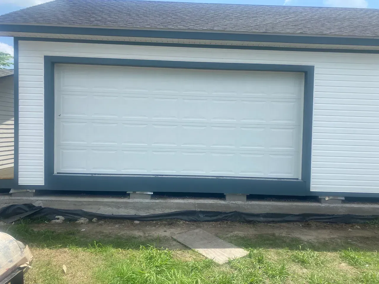 White garage door framed in dark blue on a white building, set against a grass and sky background.