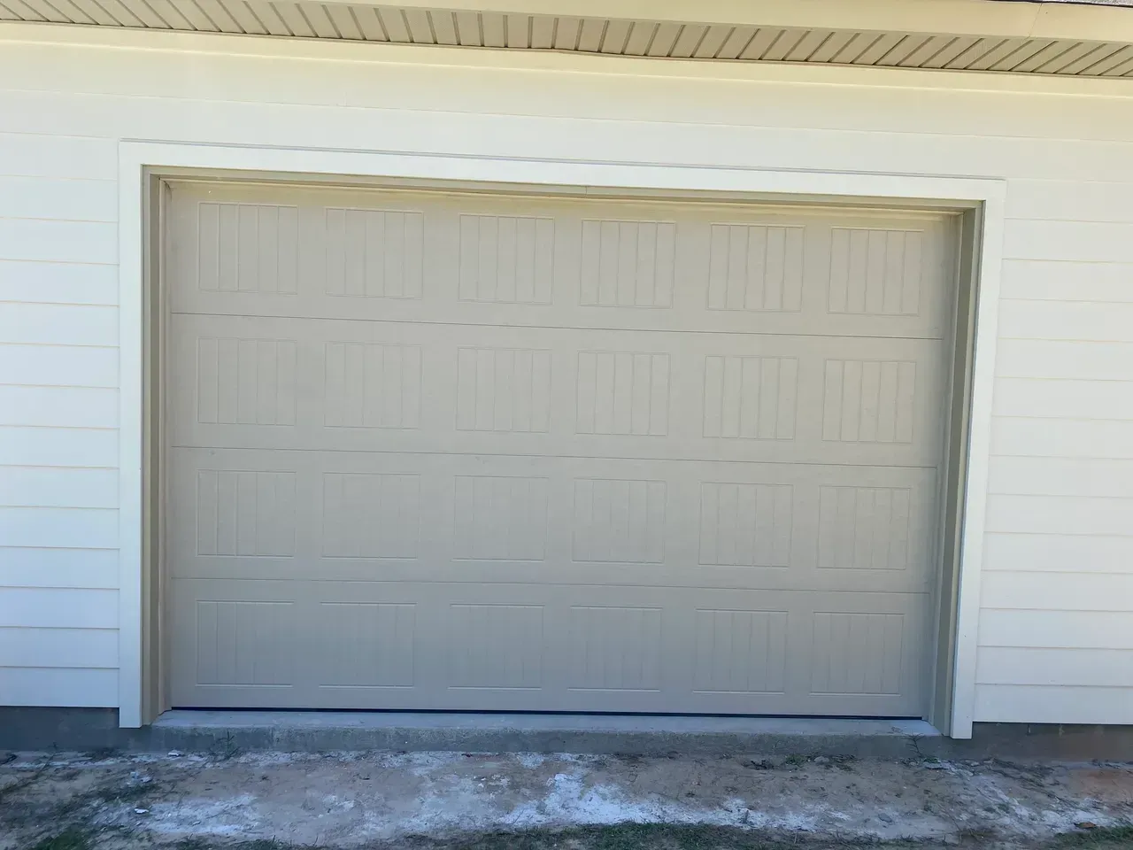 Tan closed garage door with white trim, on a white building exterior.