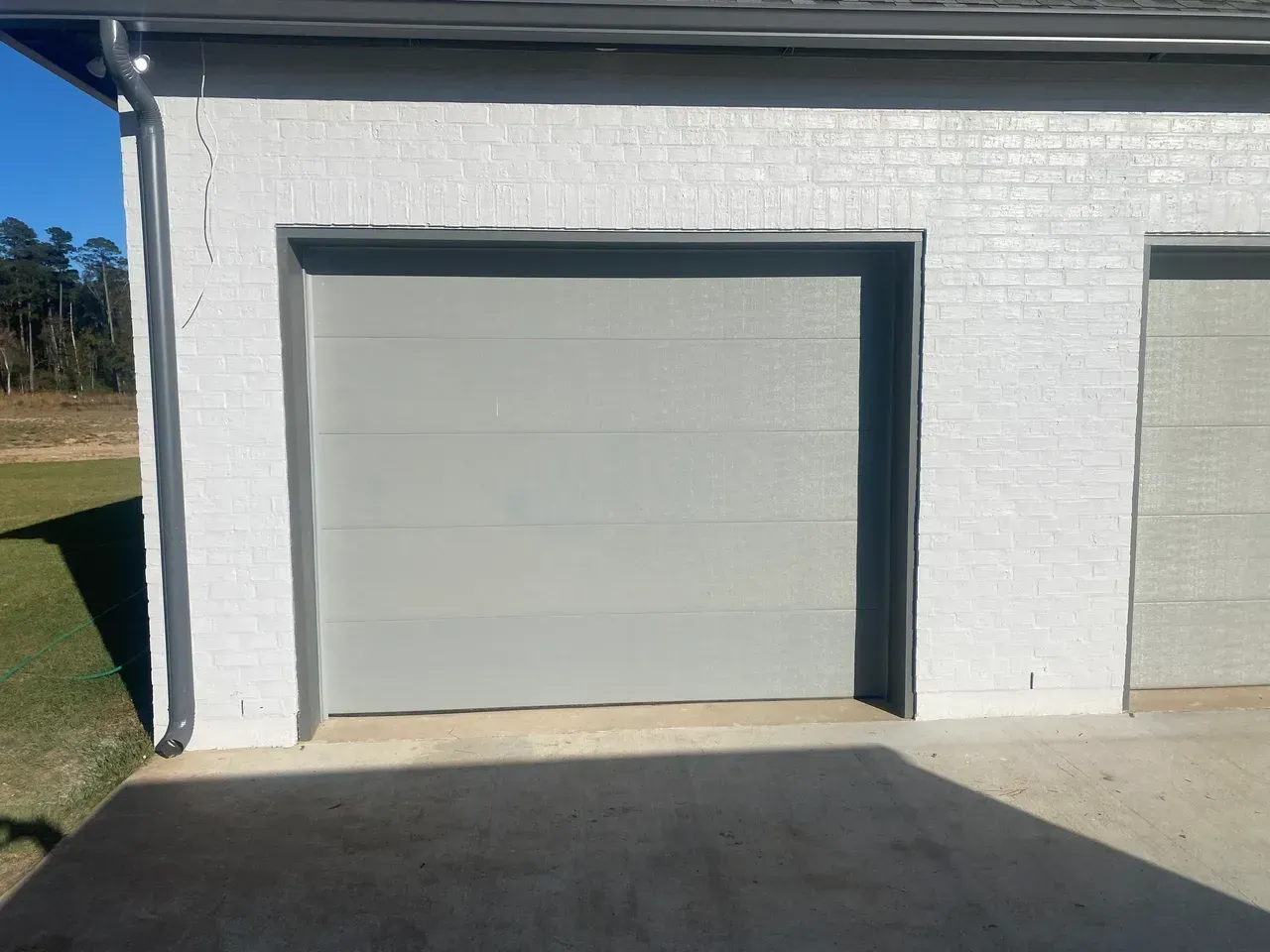 Gray garage door in white brick building, bright sunlight.