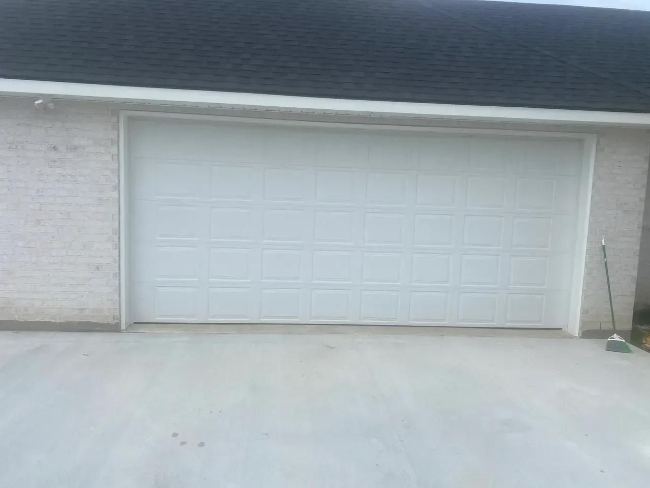 White garage door on a brick building with a dark roof. Concrete driveway.