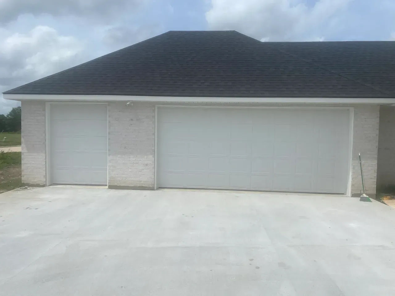White garage doors on a light brick house with a dark roof.