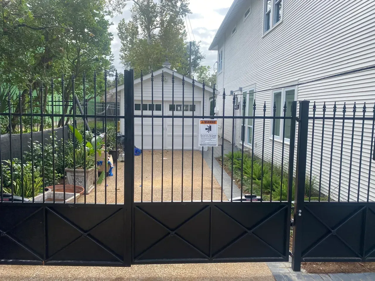 Black iron gate in front of a driveway leading to a white garage, next to a white house.