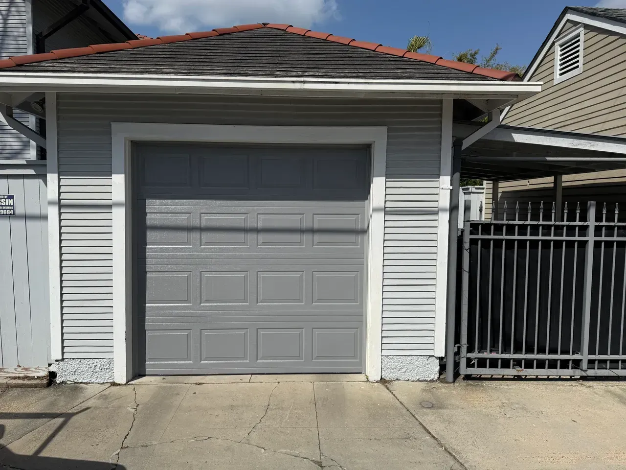 Gray garage with a closed door, light gray siding, and a red-tiled roof.