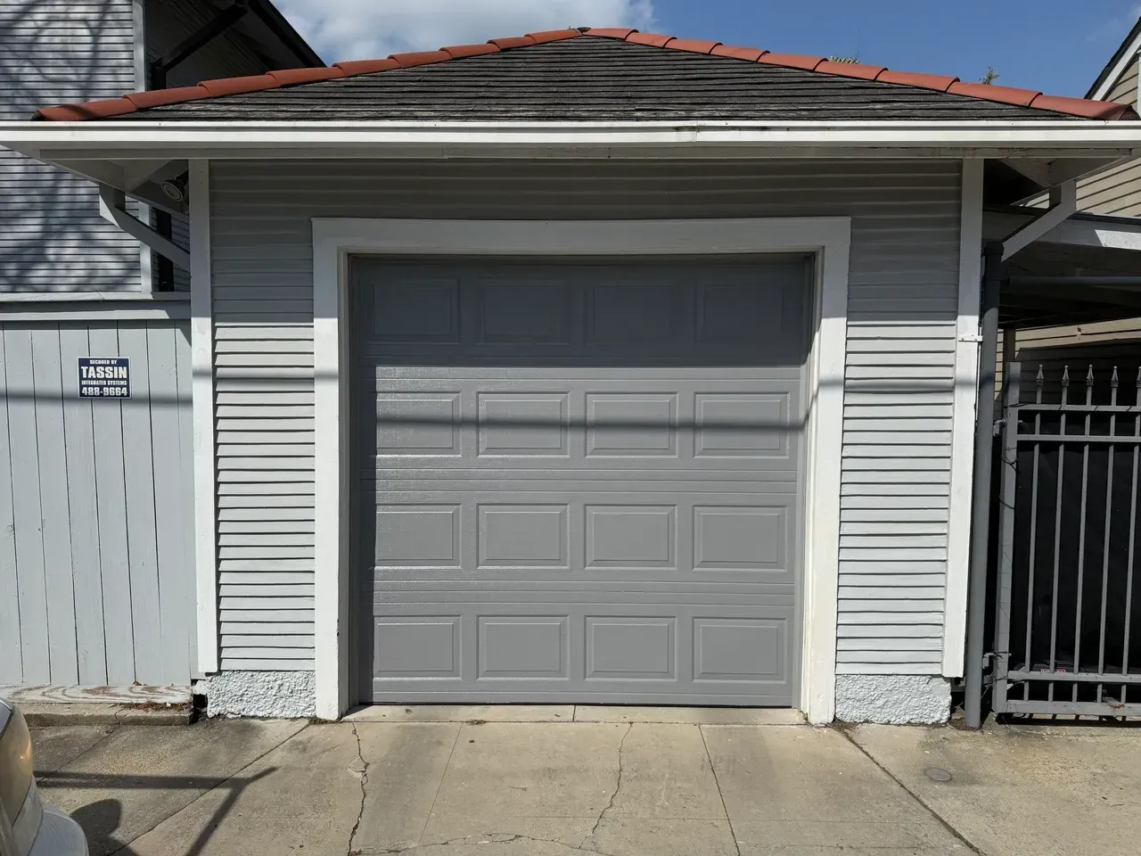 Gray garage with matching door, under a small roof, on a cracked concrete driveway.