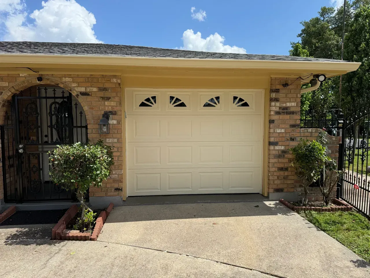 Tan garage door with decorative top windows, beige trim, brick facade.