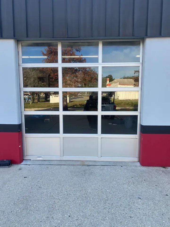 Glass garage door with white frame reflecting a street scene and the sky.