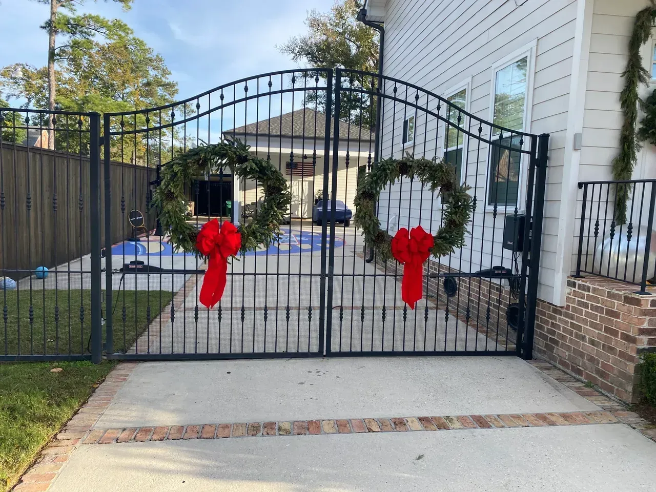 Black iron gate with wreaths and red bows, leading to a house, decorated for the holidays.