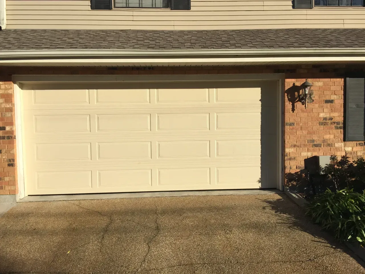Beige garage door on a brick house with a gravel driveway.