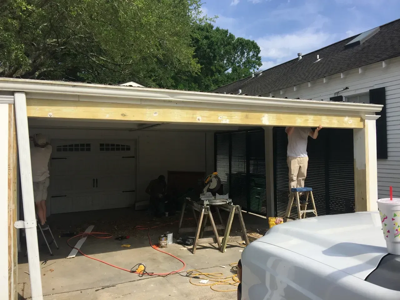 Construction workers installing a wooden header above a garage door opening; tools and supplies are visible.
