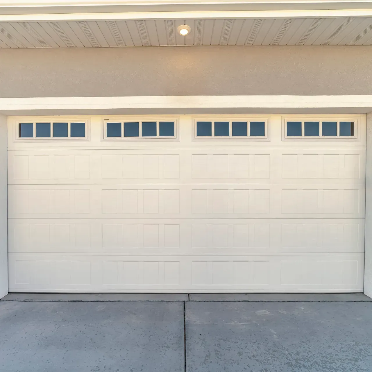 White garage door with rectangular windows above, on a beige building, grey driveway.