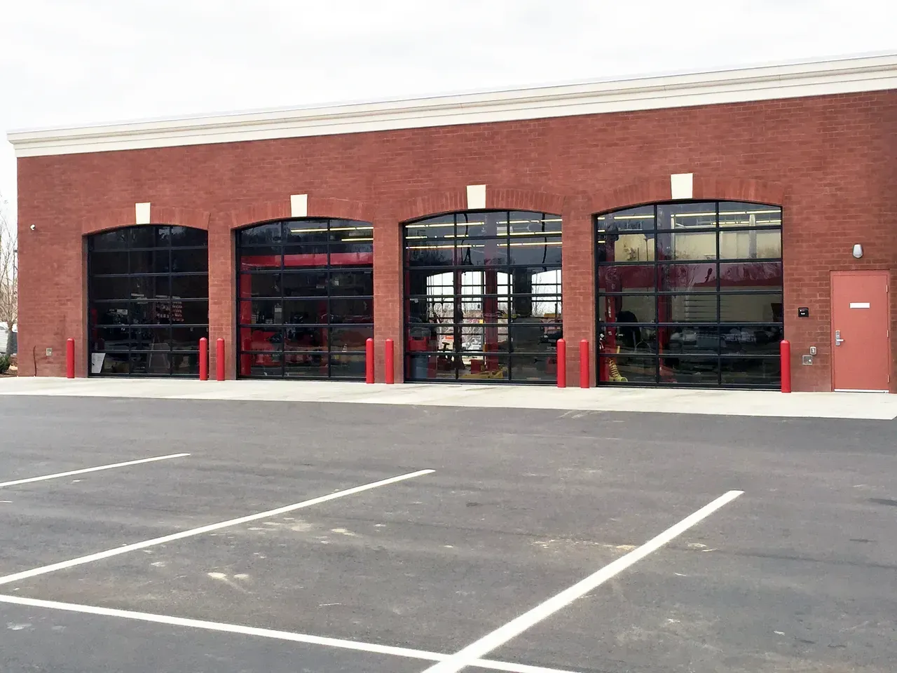 Fire station with four bay doors; red brick exterior, black glass doors, paved parking area.