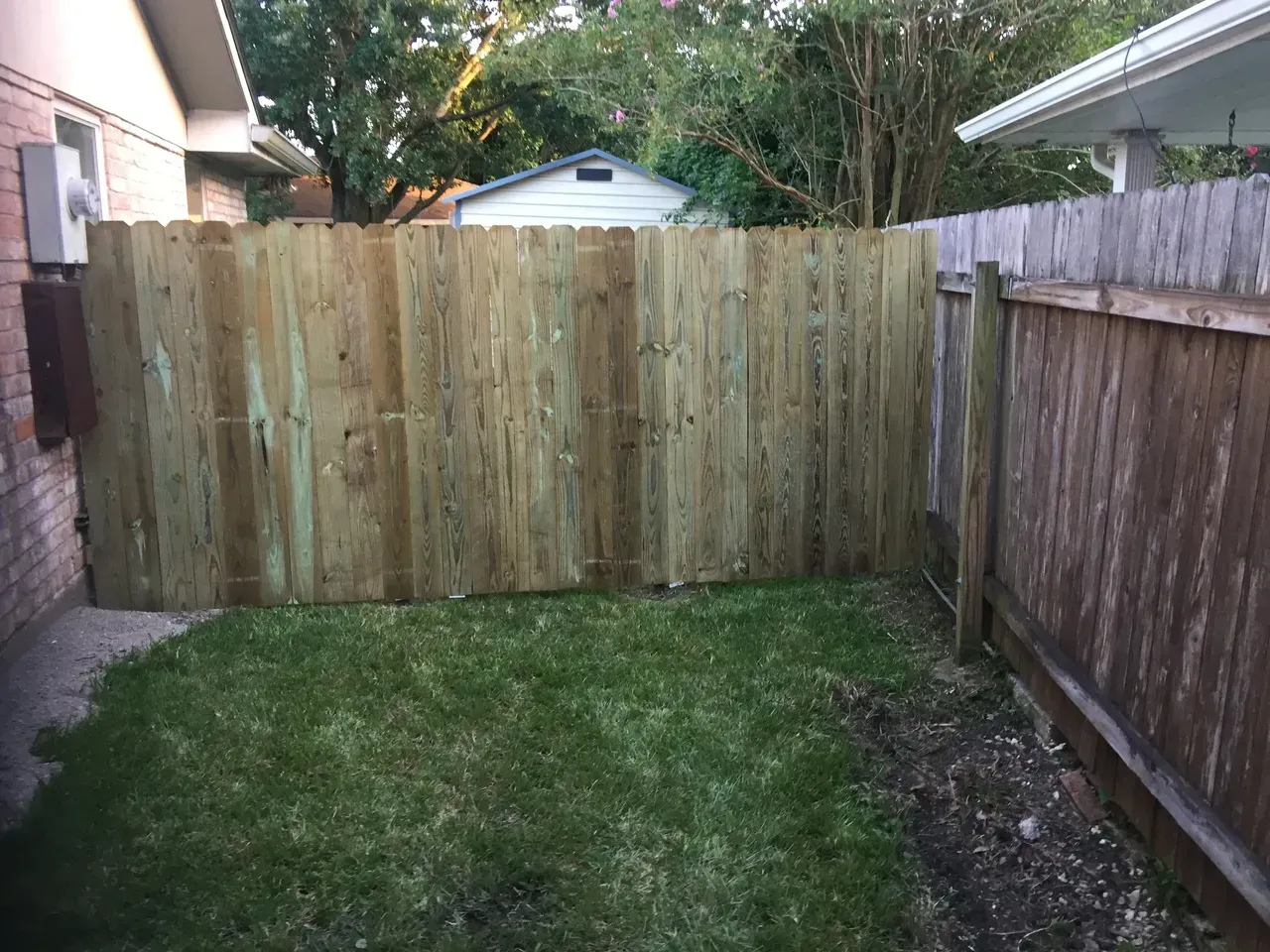 Wooden privacy fences enclose a small patch of grass. A brick wall and other fence are visible.
