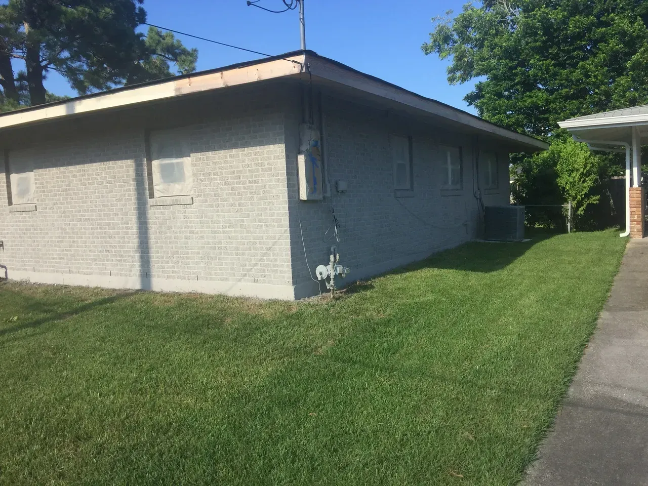 Gray brick building with green grass, sidewalk, and trees.