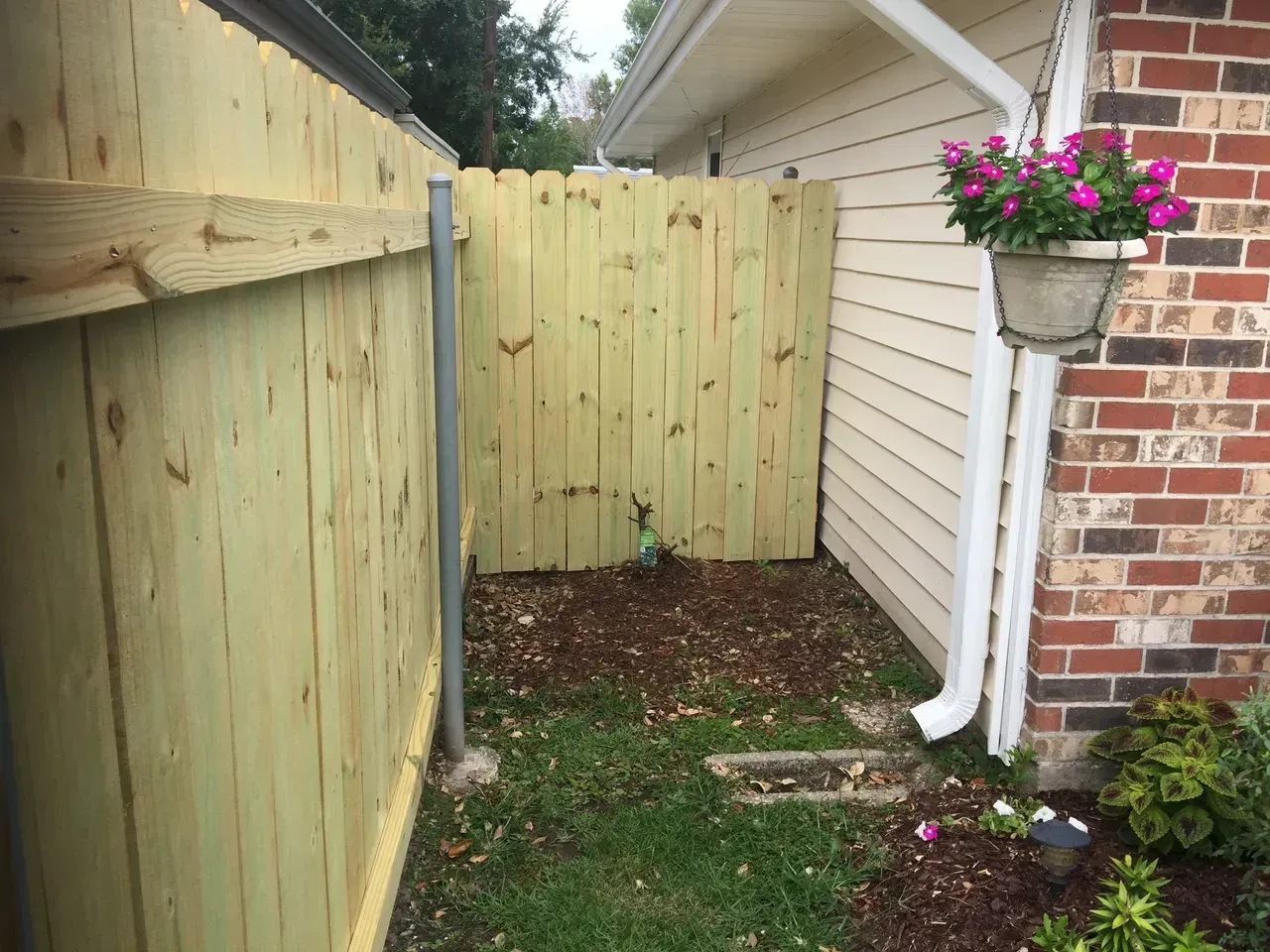 Wooden fence with a gate beside a building with a hanging flower pot.