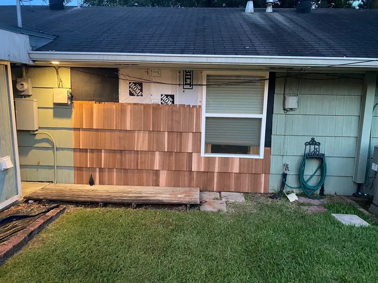 Exterior house wall with new cedar shingles and a window. A water hose and light are also visible.
