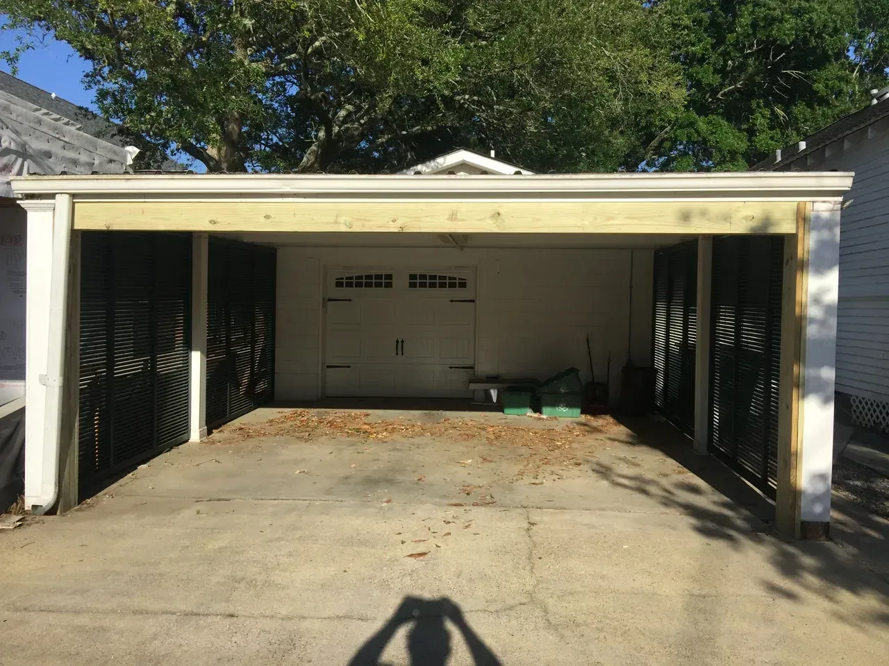 Carport with white garage door, concrete driveway, and wooden beams.