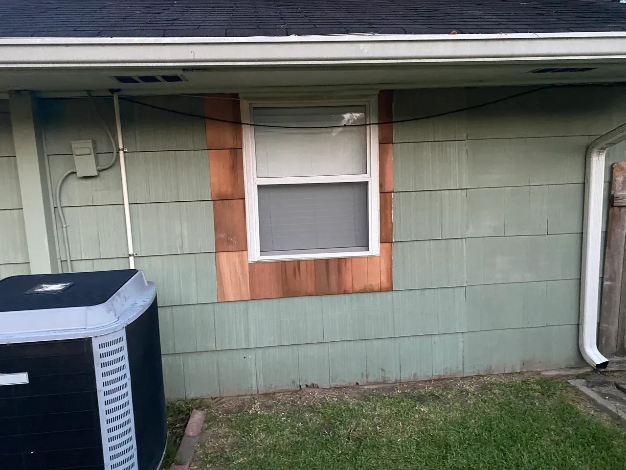 Exterior house wall with window and weathered green siding. Copper-colored wood surrounds the window.