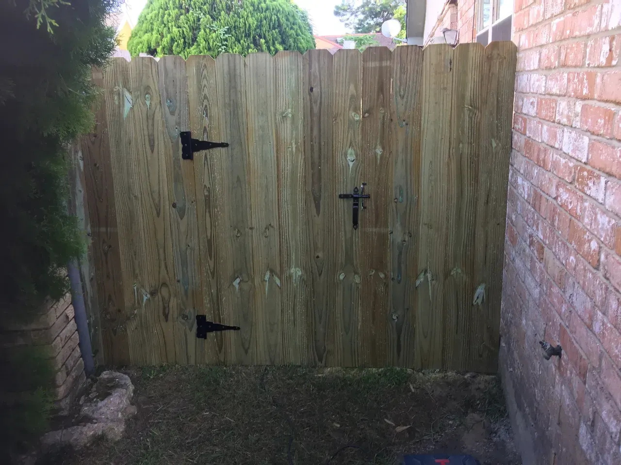 Wooden fence with black hinges and latch, attached to brick wall.
