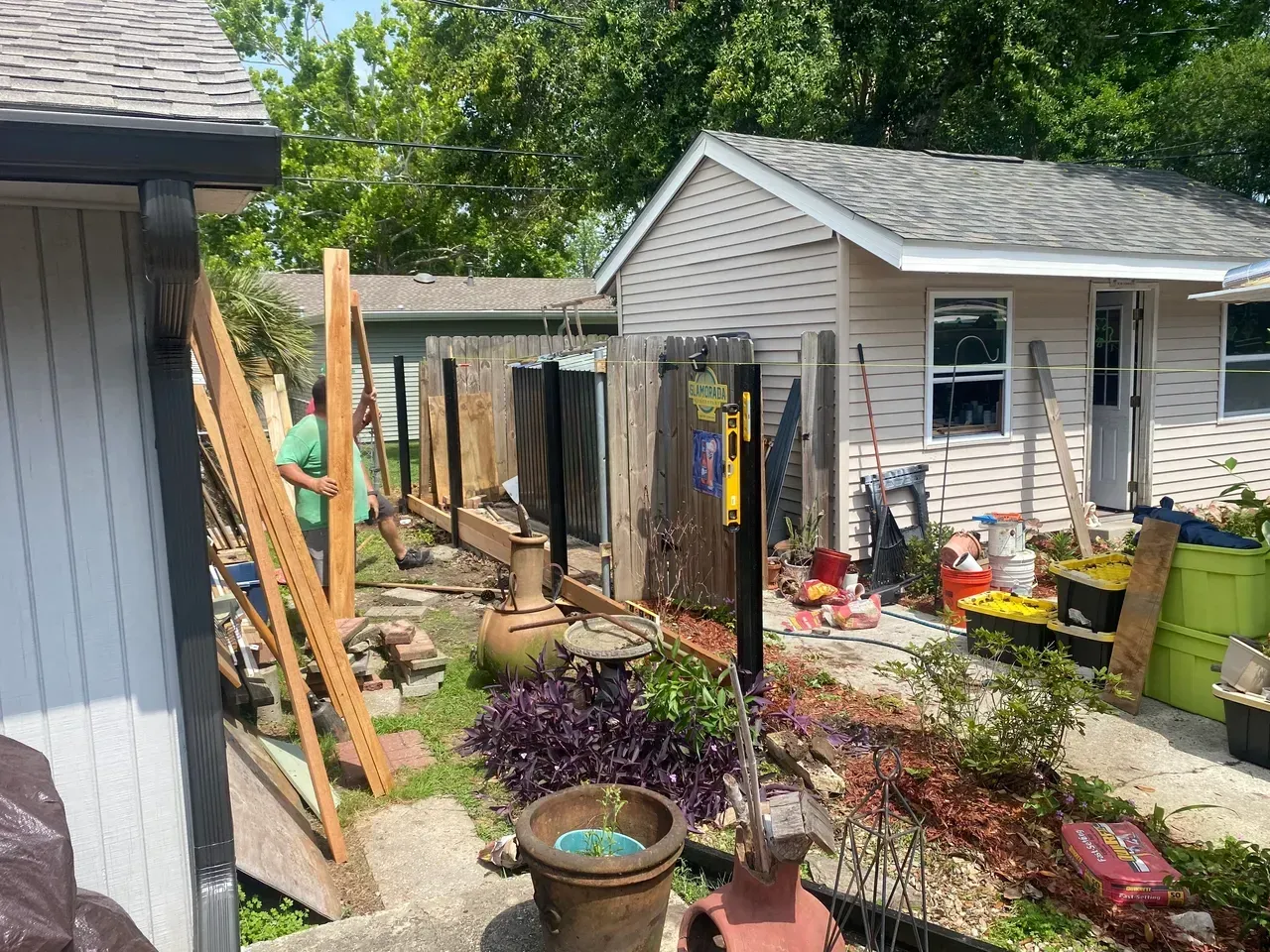 A person near a partially constructed wooden fence in a cluttered backyard with a shed.