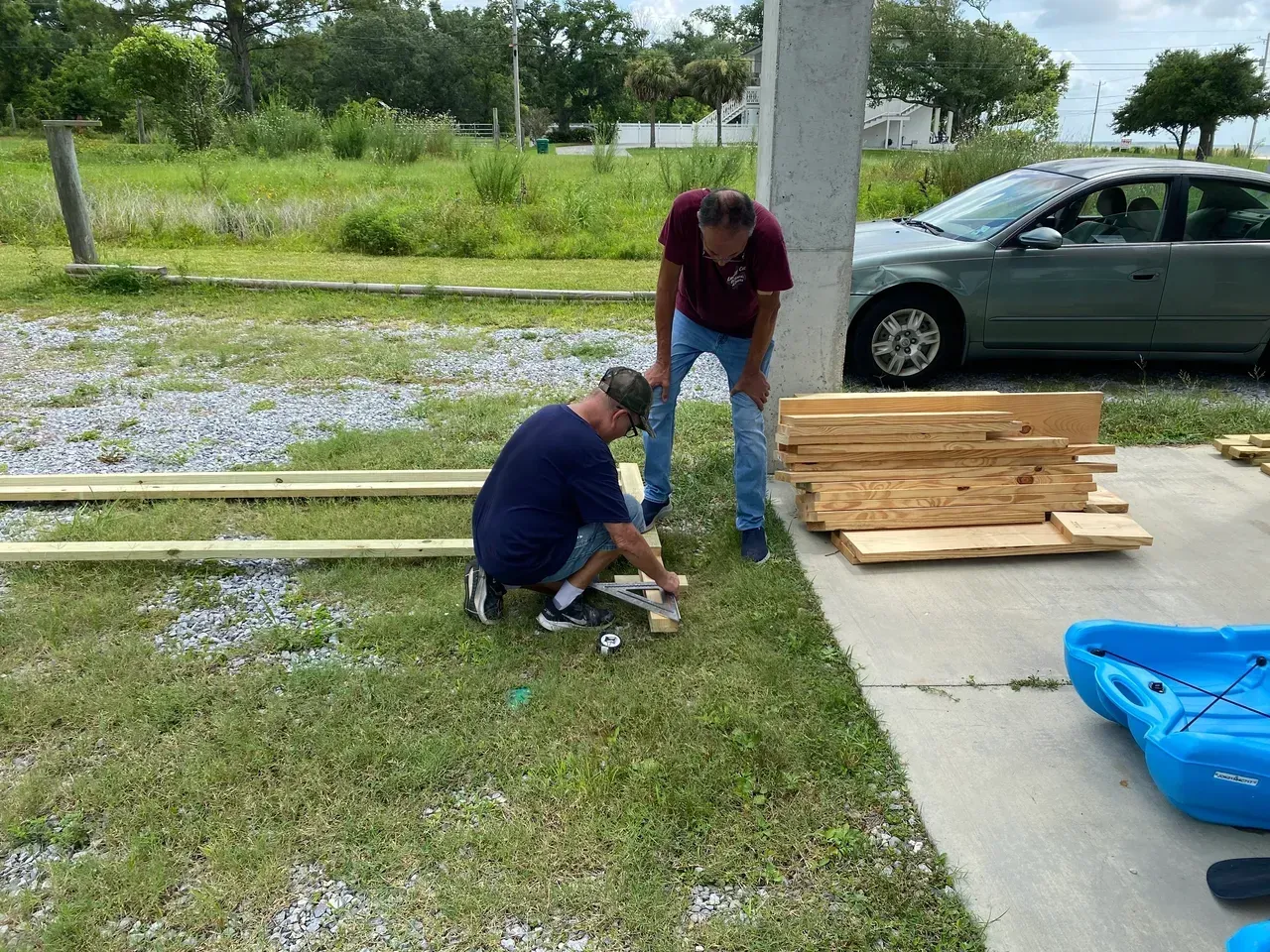 Two men assembling wood outdoors next to a car and a blue kayak.