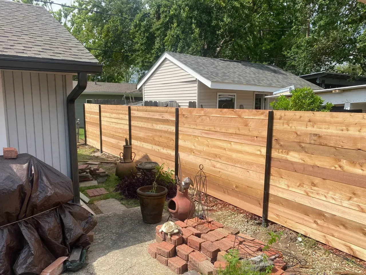 A wooden horizontal fence in a backyard, with a small house in the background.