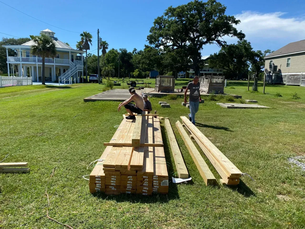 Two people with lumber on a grassy lot. A two-story house is in the background.