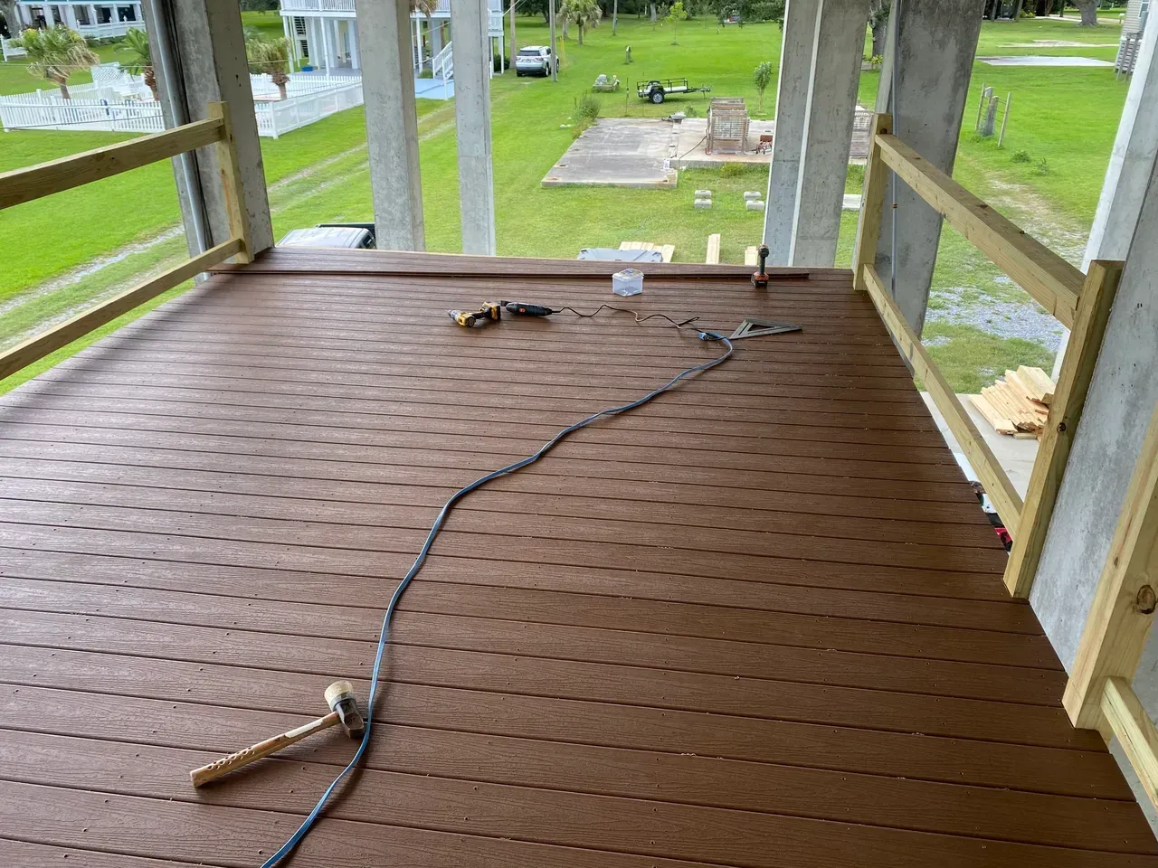 Brown deck with tools and railing, overlooking a green lawn under construction.