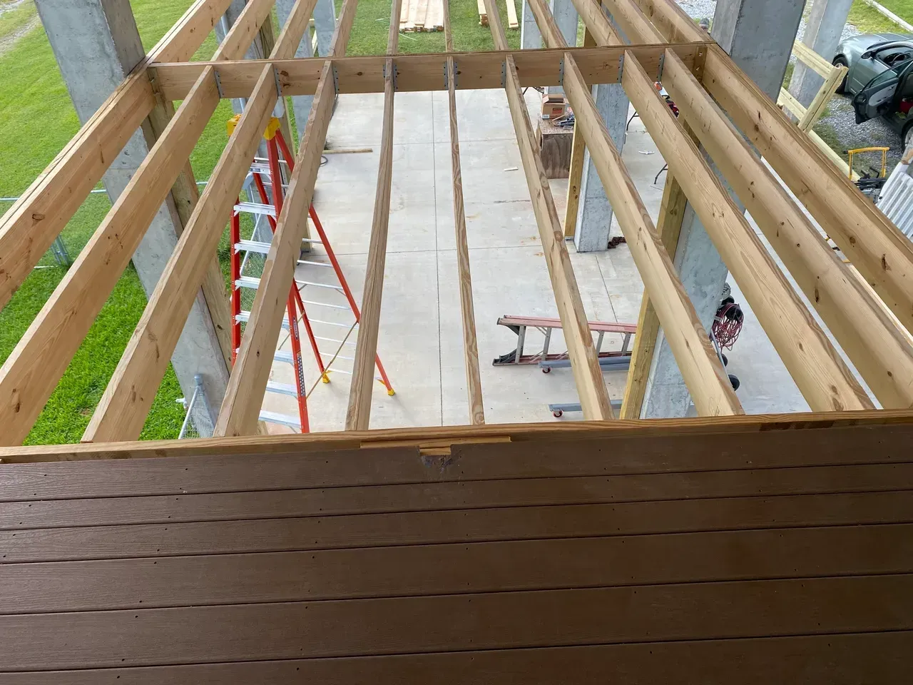 Wooden deck under construction with exposed beams. A ladder and other tools are in the background.