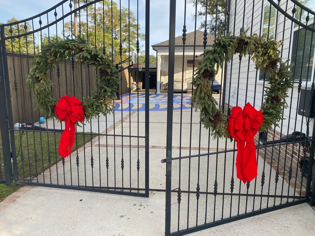 Black metal gate with green wreaths and red bows, leading to a house.