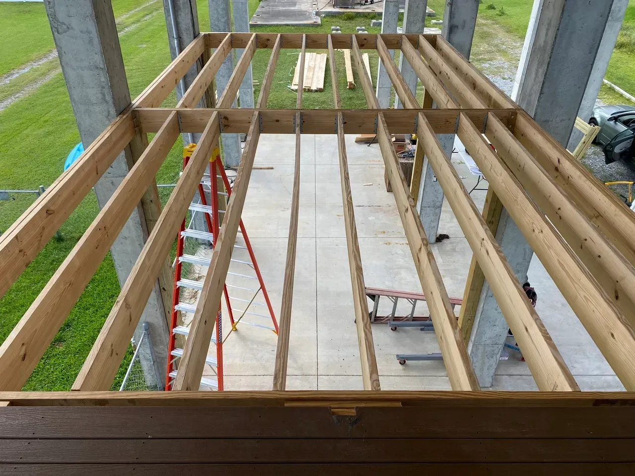 Wooden deck framing under construction, between concrete pillars.