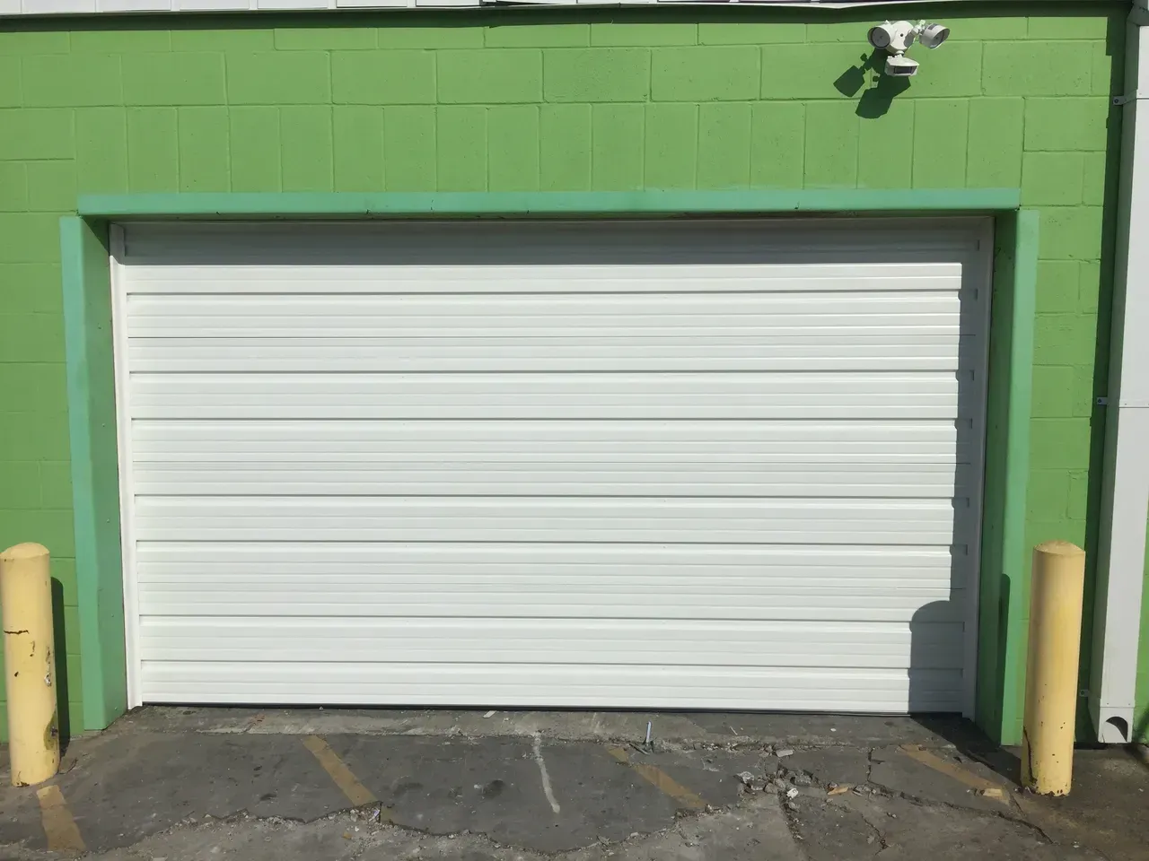 White garage door in a green building with yellow posts, under sunlight.