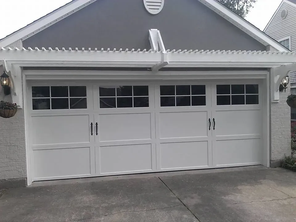 White garage door with windows, a small pergola, and side sconces.