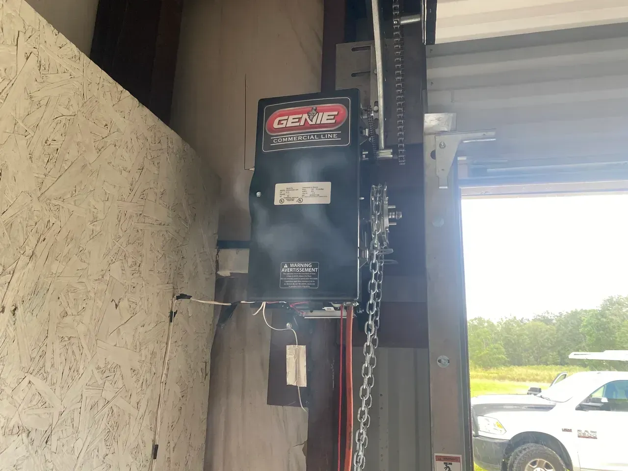 Garage door opener mounted on a wall with chain and a car visible outside.