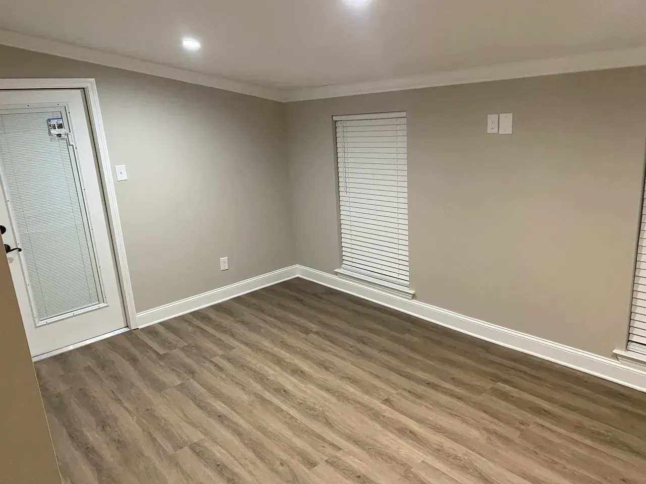 Empty room with wood-look flooring, light beige walls, white trim, and a door with a window.