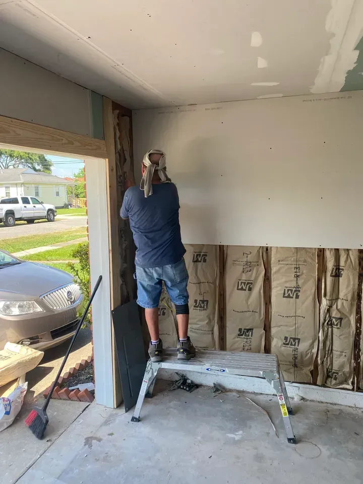 Person stands on step stool, working on drywall inside a building's entrance.