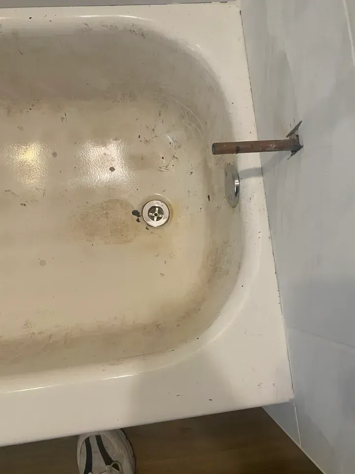 Dirty, stained white bathtub with rust-colored shower arm and drain.