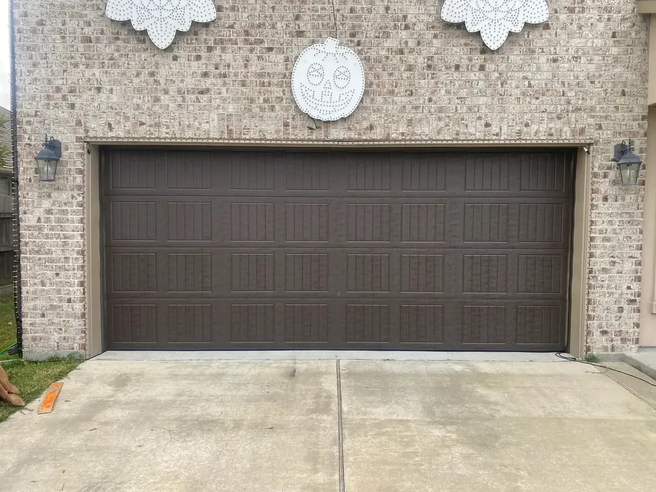 Brown garage door on a brick building with a concrete driveway. Decorative white accents above the door.