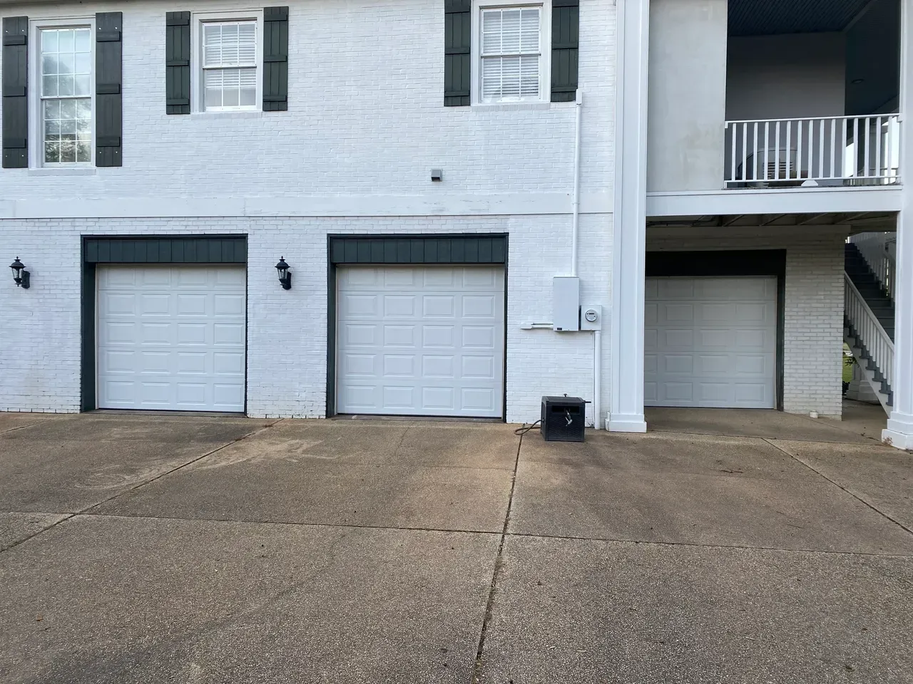 Three white garage doors on a brick building, with a balcony above one.