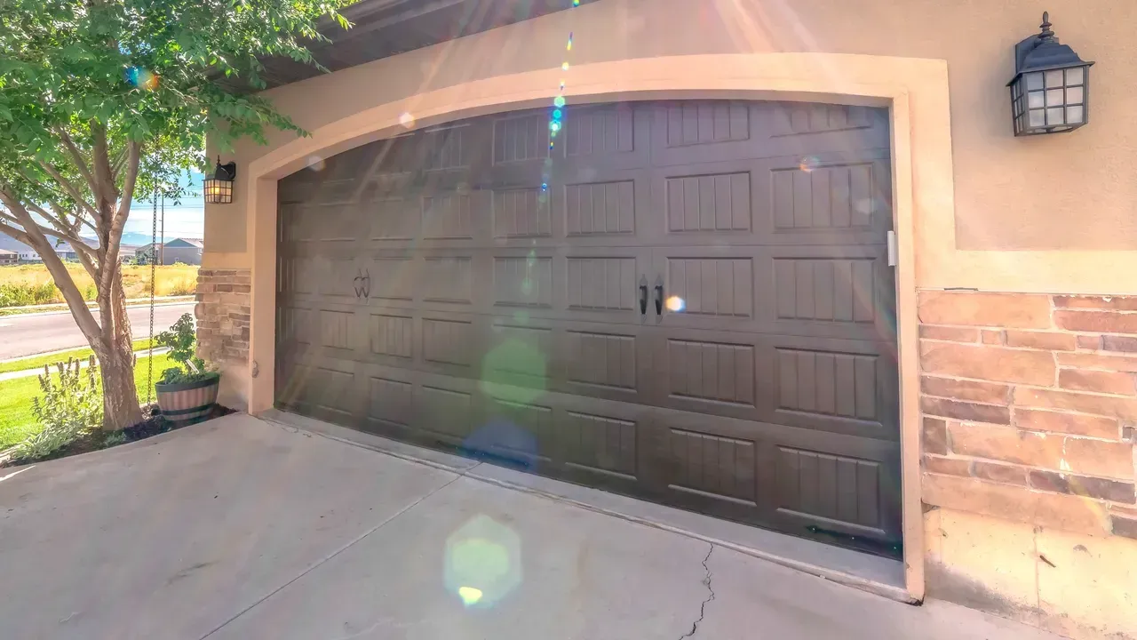 Dark brown garage door with arch, concrete driveway, stone facade, and a tree.