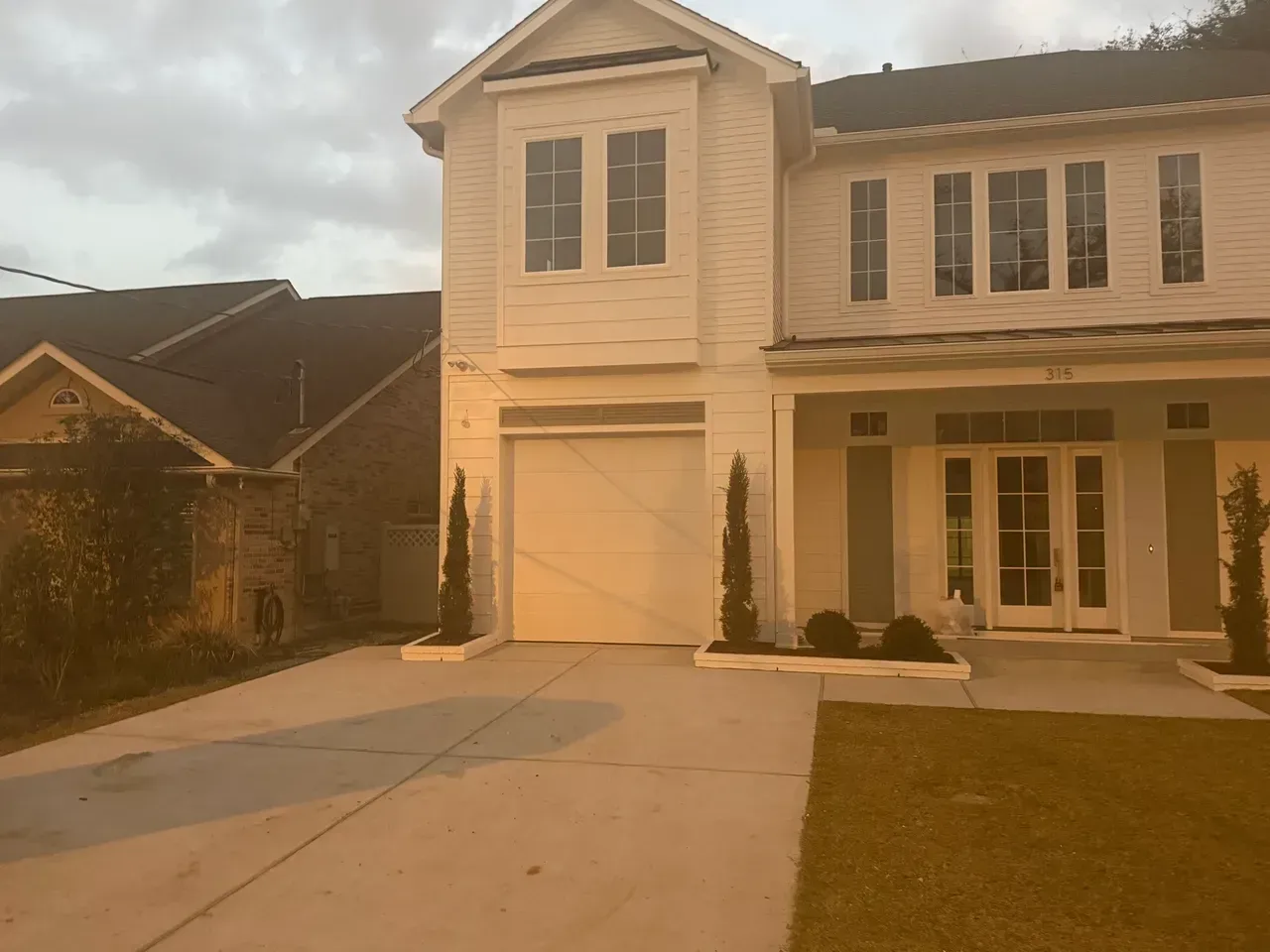 Two-story white house with a garage and double doors.  Gray driveway, green grass, and small trees.